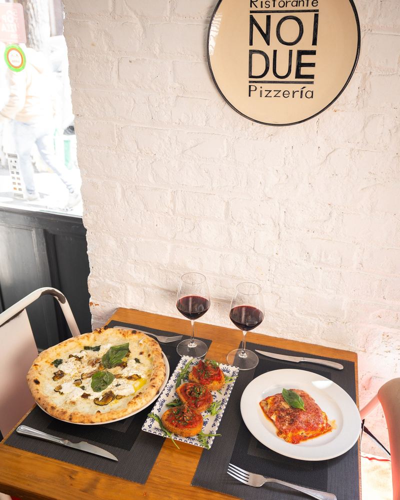 Mesa para dos bajo el rótulo de Noi Due, con pizza y vino tinto