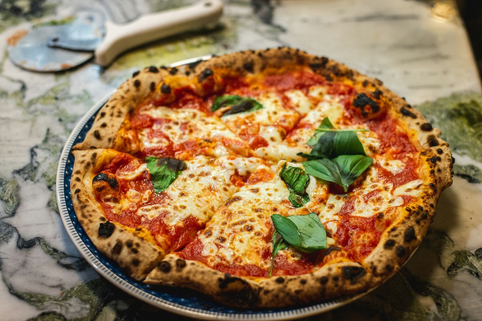 Margherita recién hecha, cornicione oscuro y albahaca fresca, sobre mesa de mármol