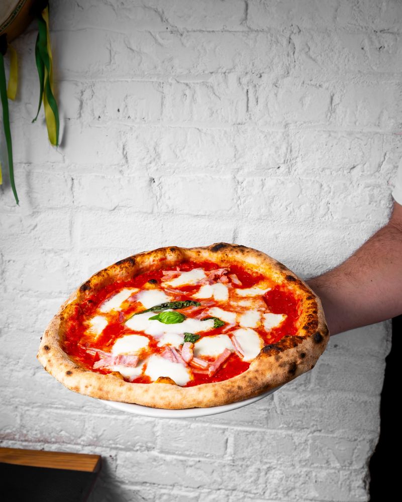 Pizza Prosciutto recién hecha, sobre la pared de ladrillo blanco